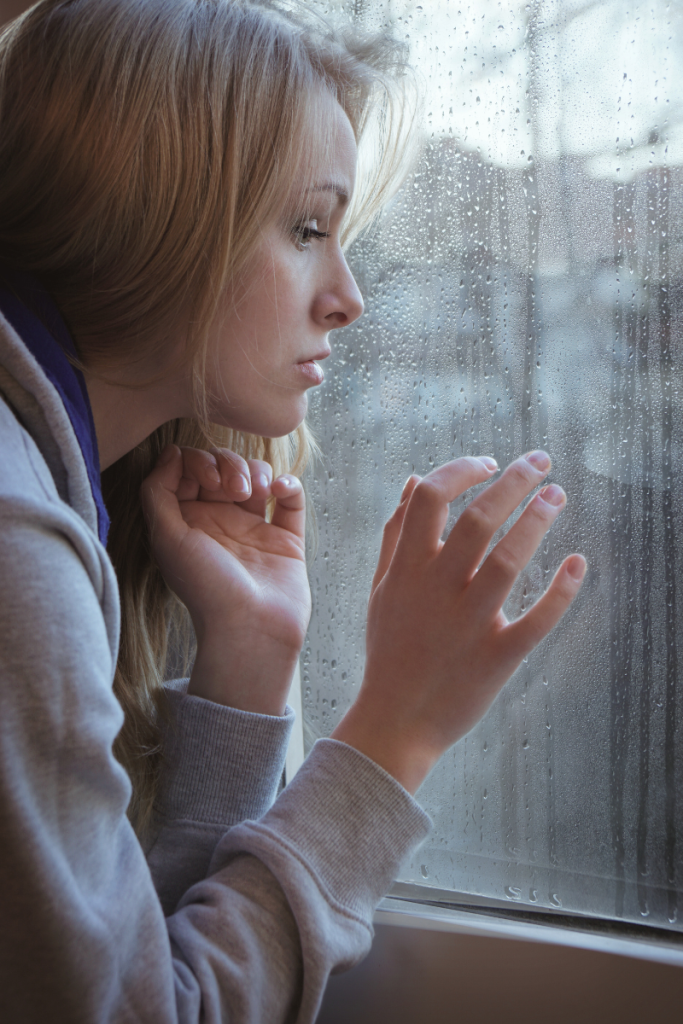female looking out window, rain, seasonal depression