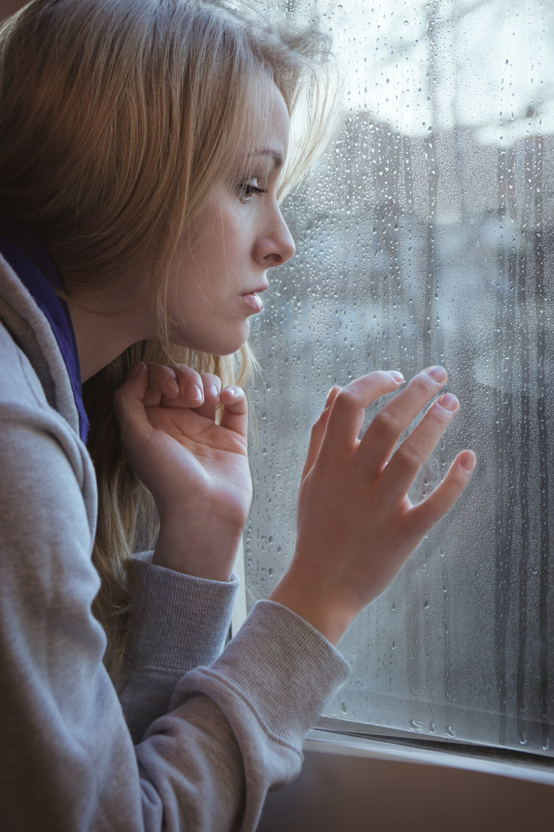 female looking out window, rain, seasonal depression